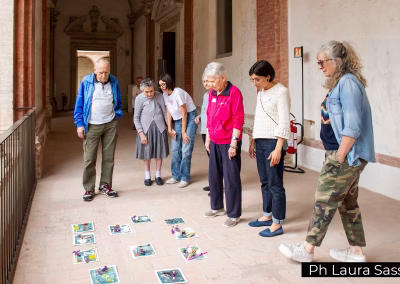 Anziani e operatori osservano insieme un'attività creativa sul pavimento di un chiostro, progetto museale inclusivo